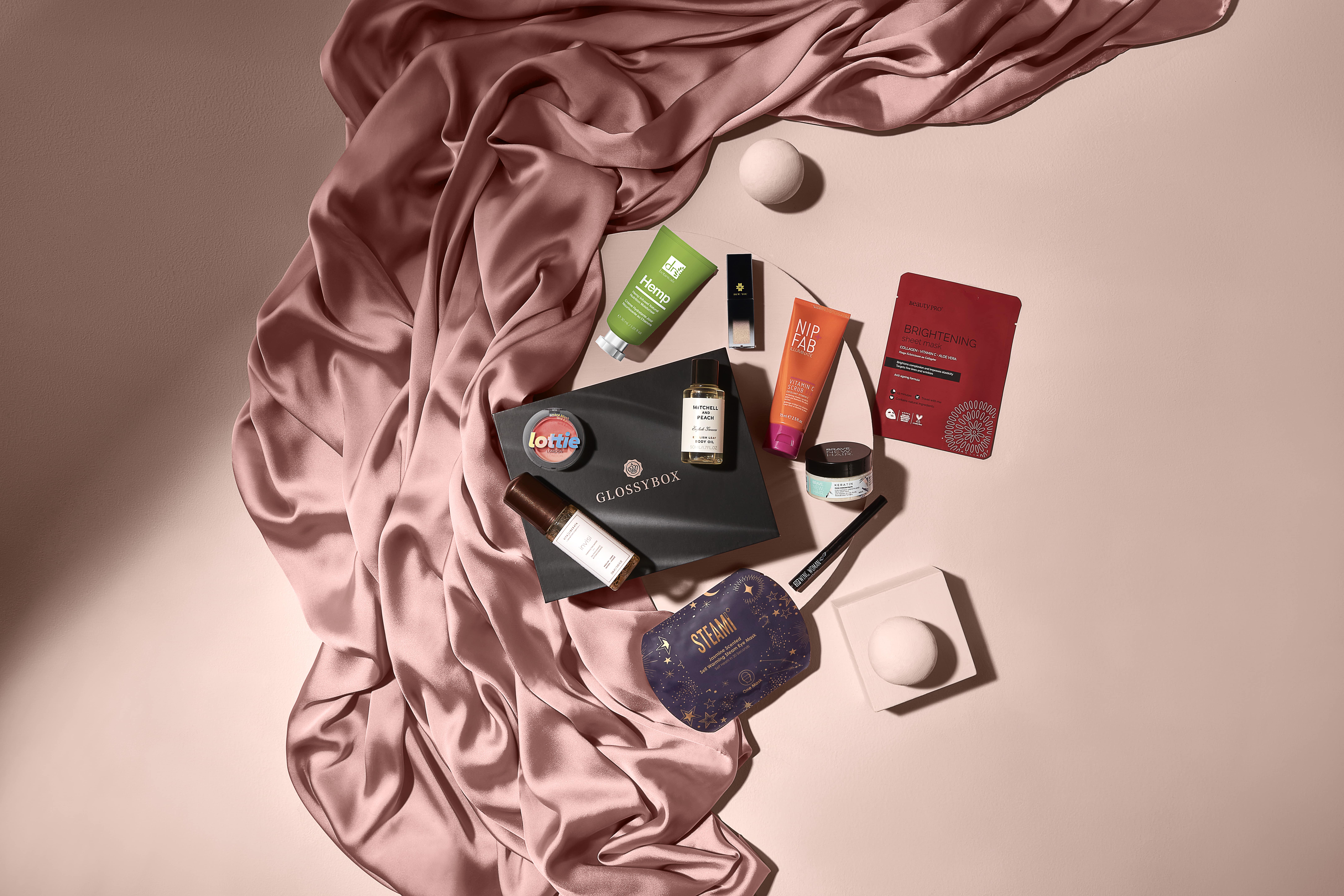 Beauty products on pale pink surface surrounded by silky pink fabric