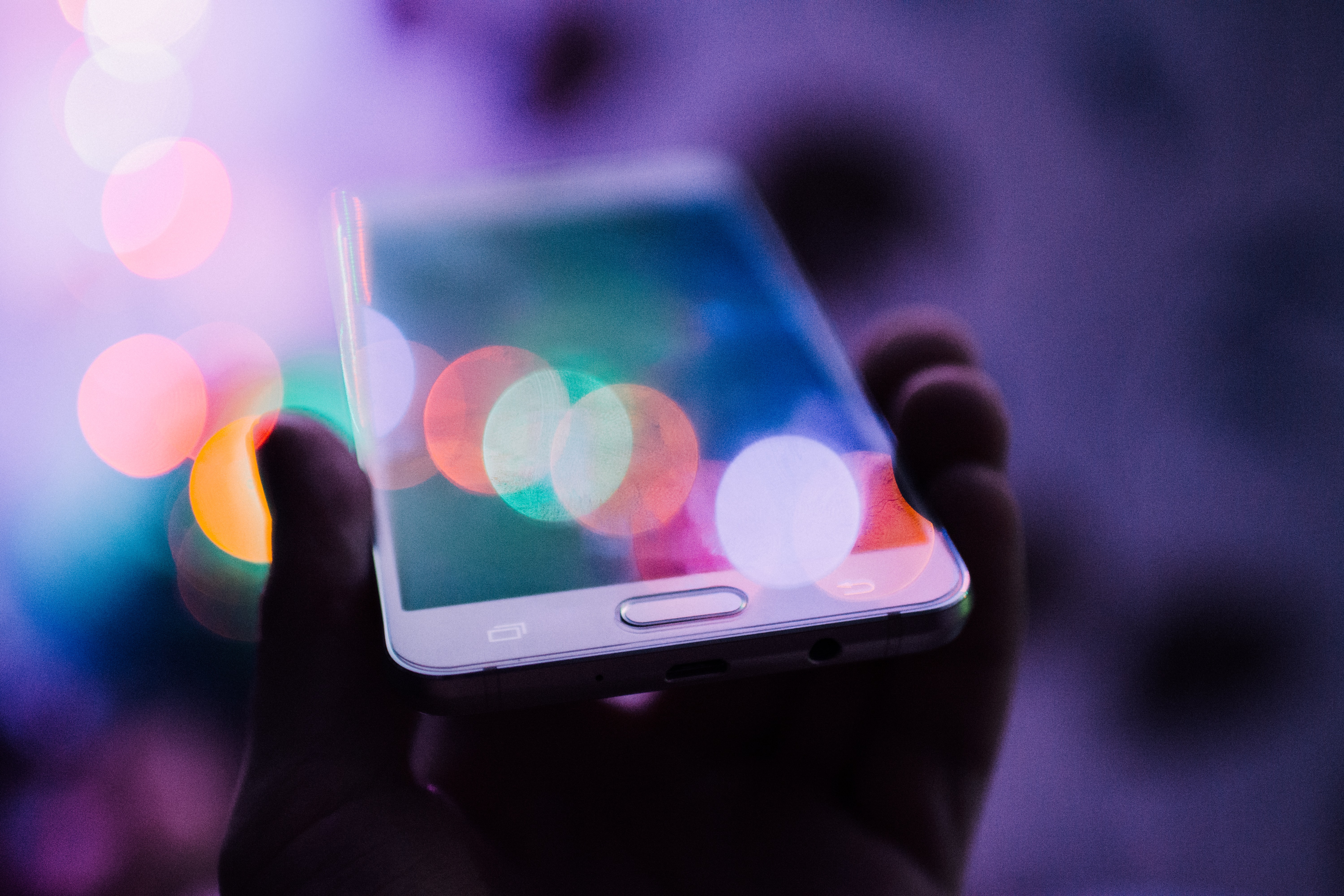 Hand holding mobile phone illuminated by multicoloured lights
